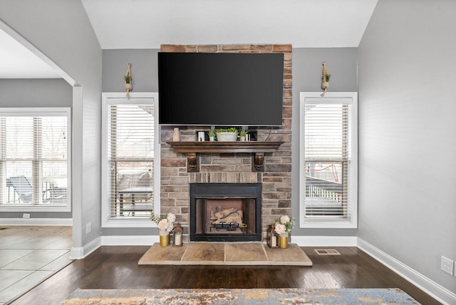 living room with visible vents, a fireplace, baseboards, and wood finished floors