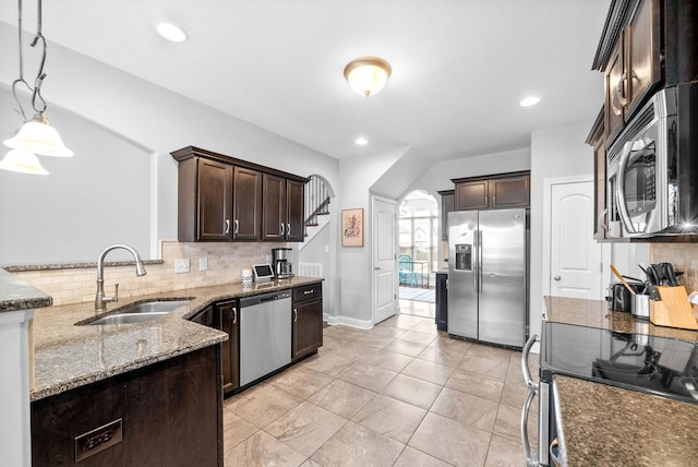 kitchen featuring arched walkways, stone counters, a sink, dark brown cabinets, and appliances with stainless steel finishes