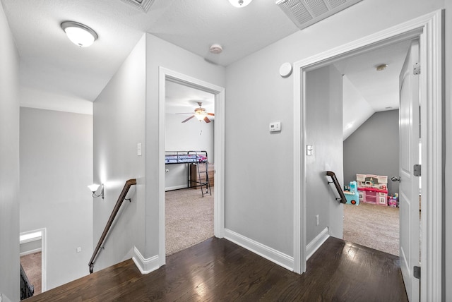 hall featuring baseboards, visible vents, dark wood-type flooring, and an upstairs landing