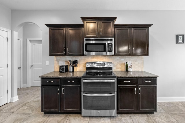 kitchen featuring tasteful backsplash, appliances with stainless steel finishes, arched walkways, and dark stone countertops