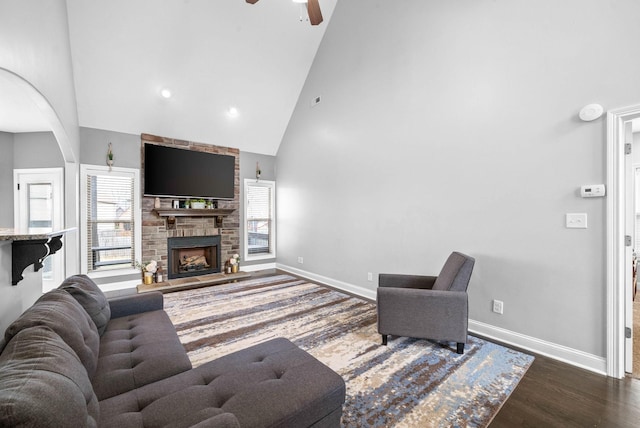 living room featuring high vaulted ceiling, a fireplace, baseboards, and wood finished floors