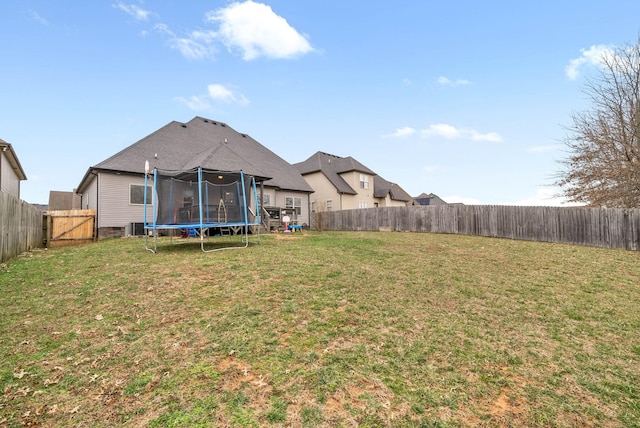 back of property with a trampoline, a fenced backyard, and a lawn