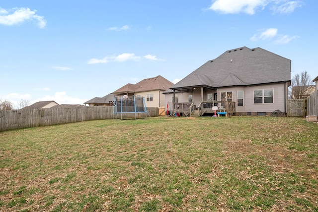 back of property featuring a fenced backyard, a shingled roof, a lawn, a wooden deck, and a trampoline