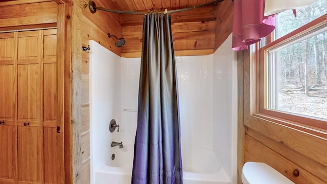 full bathroom with shower / tub combo, plenty of natural light, wood walls, and toilet