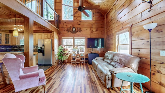 living area featuring light wood-style flooring, wood ceiling, wood walls, ceiling fan, and high vaulted ceiling