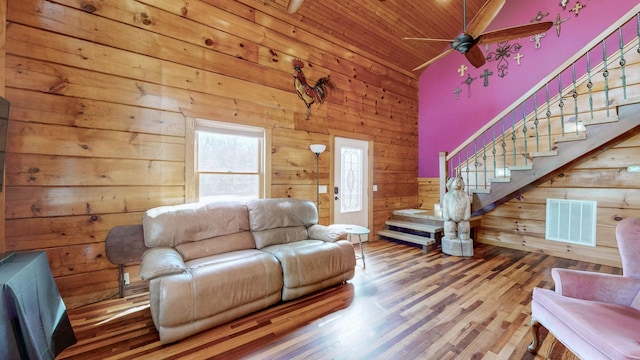 living area featuring visible vents, ceiling fan, wood walls, wood finished floors, and stairs