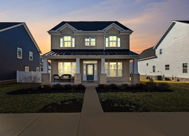 view of front of home featuring covered porch, brick siding, and a standing seam roof