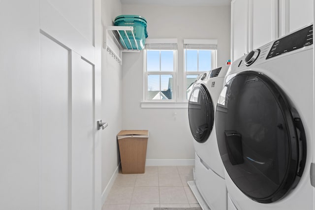 laundry area featuring washer and clothes dryer, light tile patterned flooring, cabinet space, and baseboards