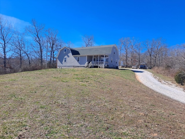 view of front facade featuring covered porch, driveway, a front lawn, and a gambrel roof