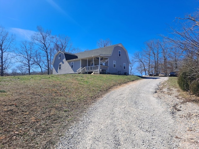 exterior space with gravel driveway, covered porch, a yard, and a gambrel roof