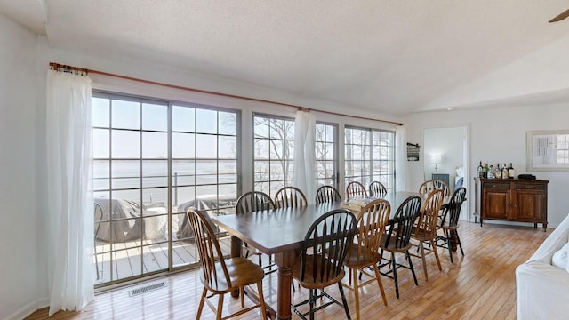 dining room featuring light wood finished floors, visible vents, vaulted ceiling, and a textured ceiling