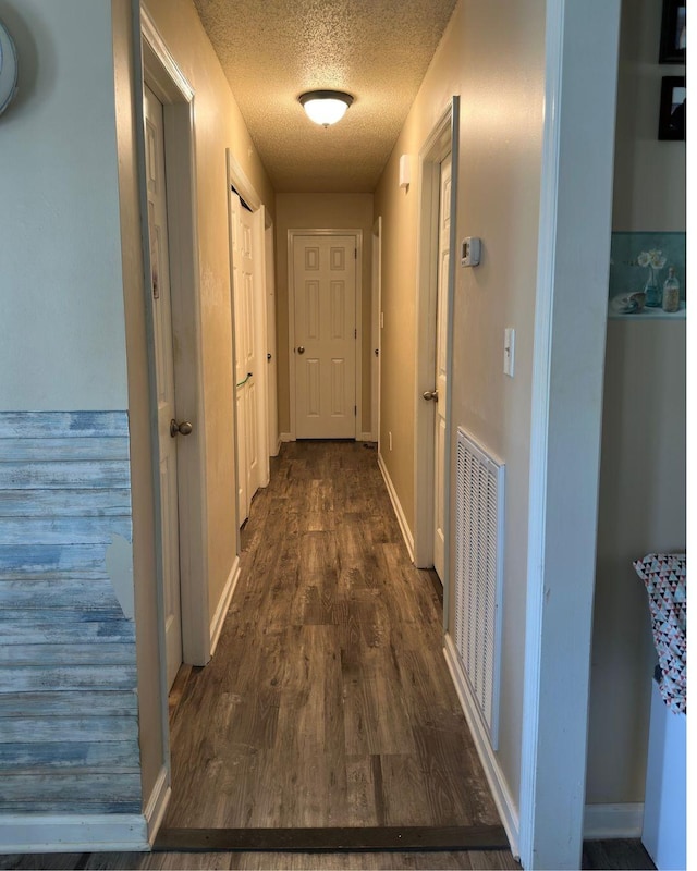 corridor featuring dark wood-style flooring, visible vents, a textured ceiling, and baseboards