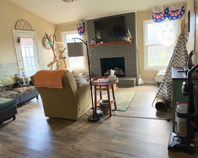 living area featuring a brick fireplace, a wainscoted wall, a textured ceiling, and wood finished floors