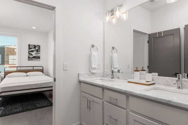 ensuite bathroom with double vanity, connected bathroom, a sink, and wood finished floors