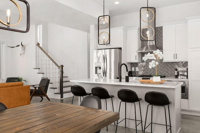 kitchen featuring a kitchen island with sink, a kitchen breakfast bar, light countertops, backsplash, and stainless steel fridge with ice dispenser