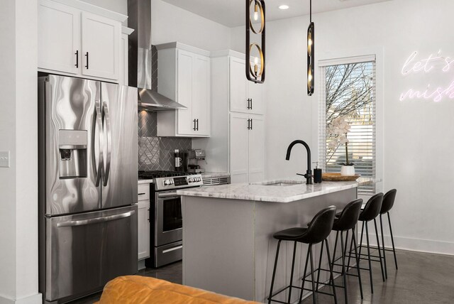 kitchen with an island with sink, wall chimney exhaust hood, backsplash, stainless steel appliances, and a sink