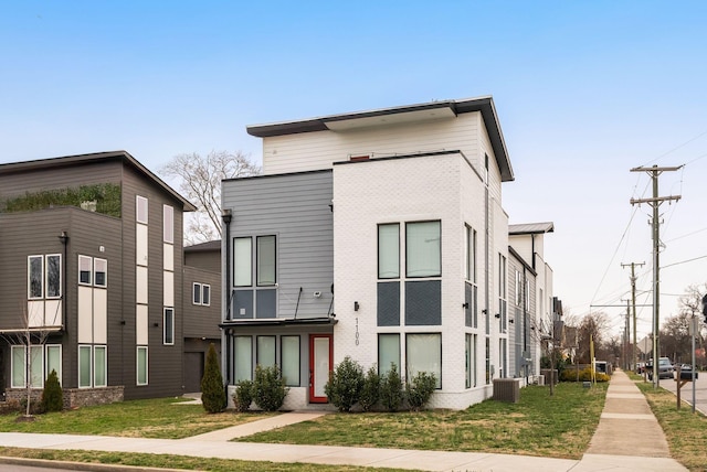 view of front facade with brick siding, central AC, and a front yard