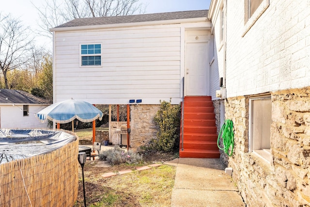 rear view of property with entry steps, stone siding, and a shingled roof