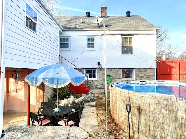back of property featuring fence, stone siding, a chimney, and a shingled roof