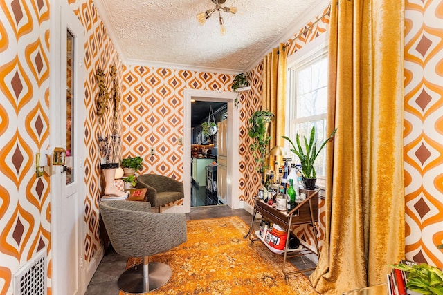 sitting room with wallpapered walls, a textured ceiling, and ornamental molding