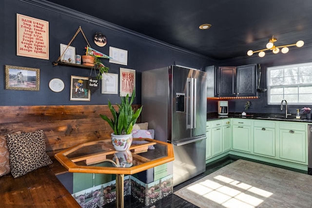 kitchen featuring crown molding, dark countertops, a sink, stainless steel appliances, and green cabinetry