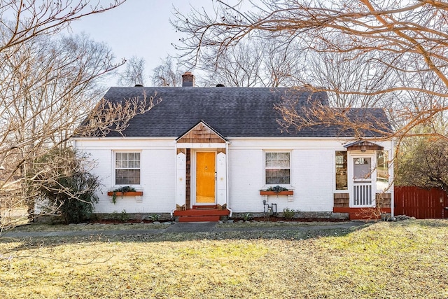 view of front facade with brick siding, a chimney, roof with shingles, fence, and a front yard