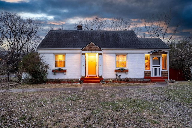 view of front of property with roof with shingles, a chimney, and brick siding