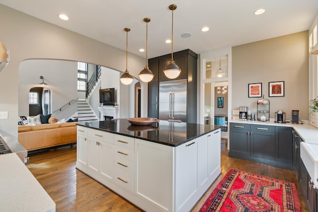 kitchen featuring arched walkways, light wood finished floors, recessed lighting, stainless steel built in fridge, and white cabinetry