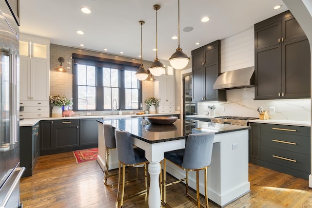 kitchen with a breakfast bar, decorative backsplash, a kitchen island, wood finished floors, and wall chimney exhaust hood