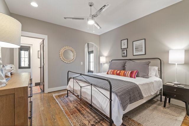 bedroom featuring light wood-style floors, arched walkways, baseboards, and a ceiling fan