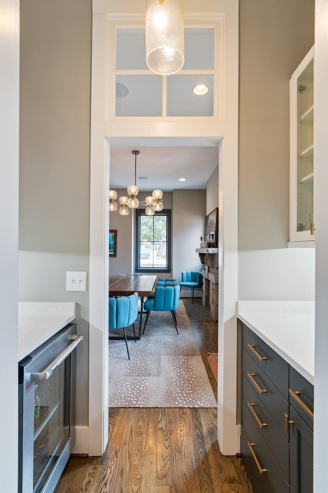 bar featuring hanging light fixtures, wine cooler, a chandelier, and dark wood-type flooring