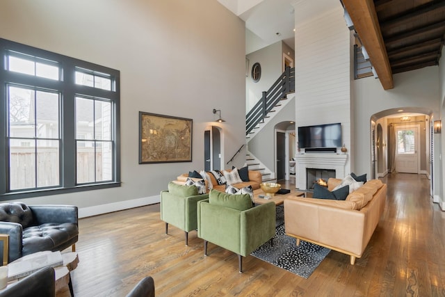 living area with arched walkways, a fireplace, a high ceiling, wood finished floors, and stairs