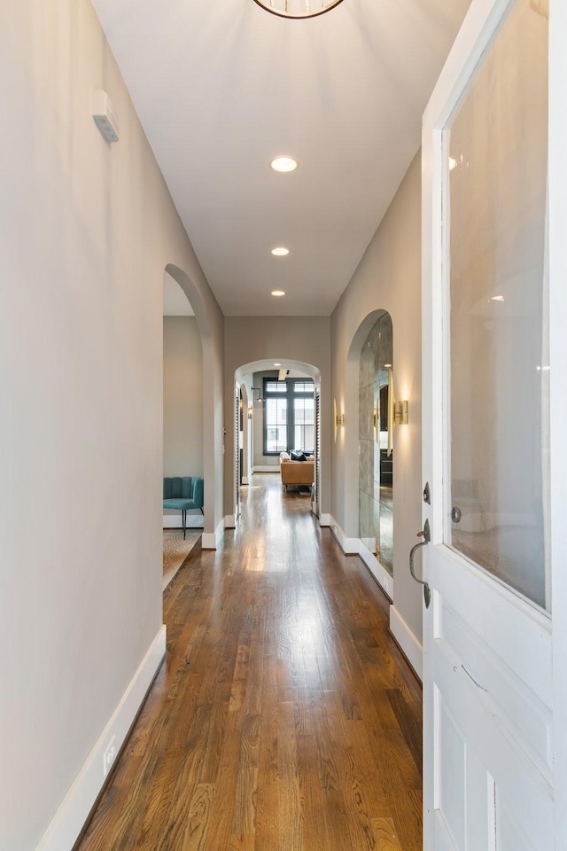 hall featuring arched walkways, dark wood finished floors, baseboards, and recessed lighting