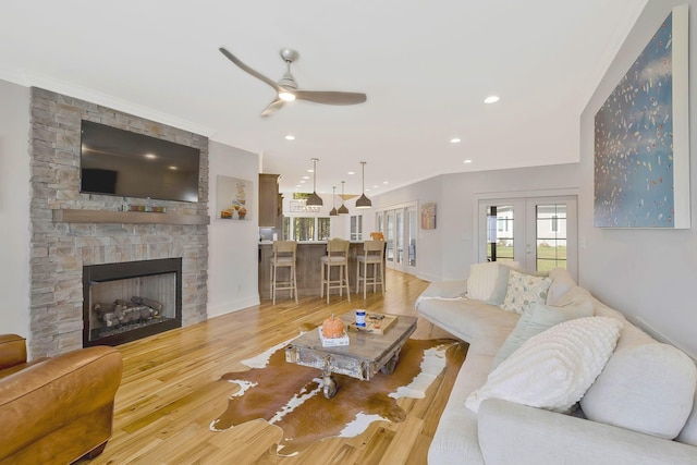 living room featuring a ceiling fan, french doors, wood finished floors, and a stone fireplace