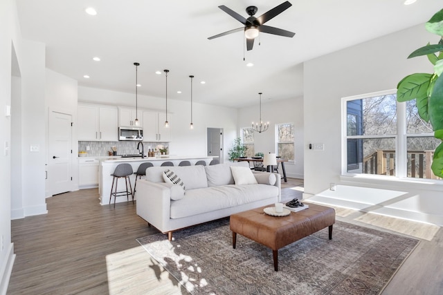 living area featuring recessed lighting, baseboards, light wood-style flooring, and ceiling fan with notable chandelier