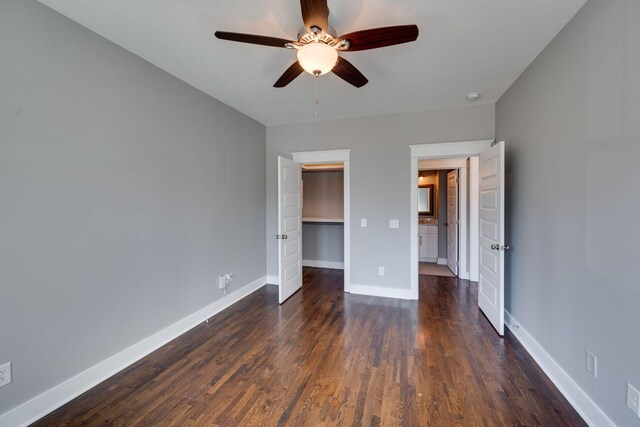 unfurnished bedroom with a spacious closet, dark wood-style flooring, a closet, and baseboards