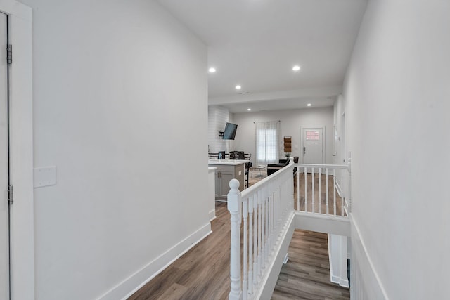 corridor with baseboards, wood finished floors, an upstairs landing, and recessed lighting