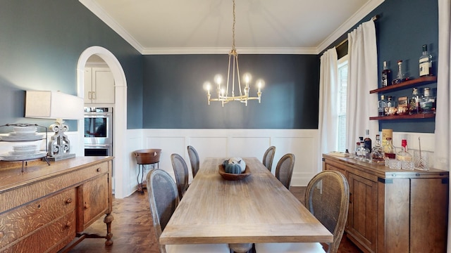 dining area featuring a wainscoted wall, a chandelier, arched walkways, and ornamental molding