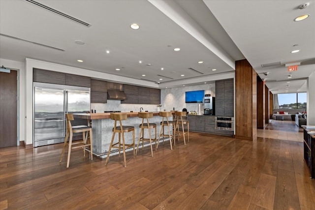 kitchen featuring dark wood finished floors, modern cabinets, a breakfast bar area, built in refrigerator, and dark brown cabinets