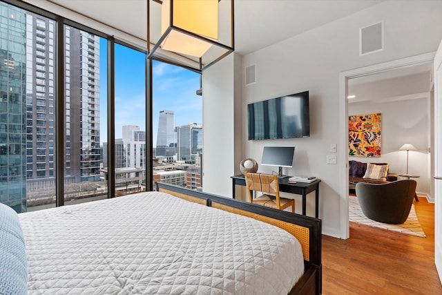 bedroom with floor to ceiling windows, visible vents, and wood finished floors