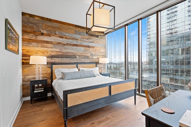 bedroom with baseboards, wooden walls, wood finished floors, and floor to ceiling windows