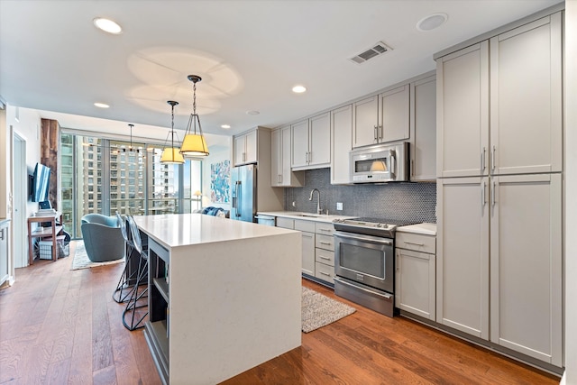 kitchen featuring gray cabinetry, visible vents, appliances with stainless steel finishes, decorative backsplash, and a center island