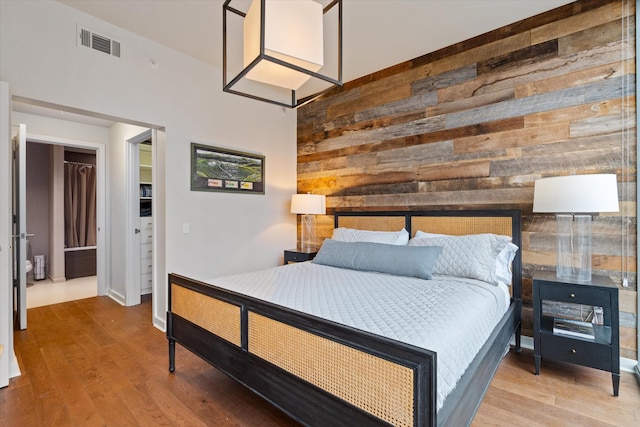 bedroom featuring an accent wall, wooden walls, visible vents, and wood finished floors