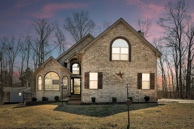 french country inspired facade with brick siding, an outdoor structure, a chimney, and a front lawn