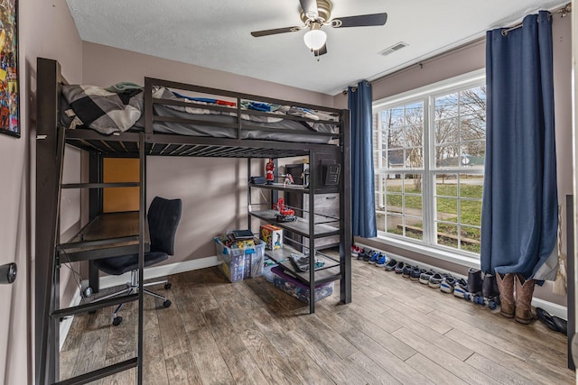 bedroom with baseboards, a textured ceiling, visible vents, and wood finished floors