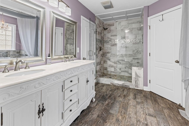 full bath with double vanity, visible vents, wood finished floors, a shower stall, and a sink