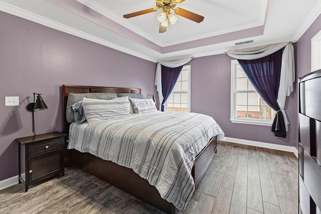 bedroom featuring visible vents, a tray ceiling, wood finished floors, and ornamental molding