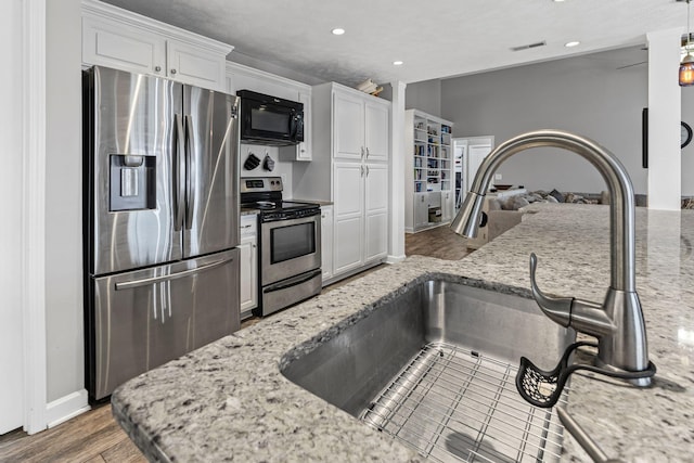 kitchen with wood finished floors, light stone countertops, stainless steel appliances, white cabinetry, and a sink