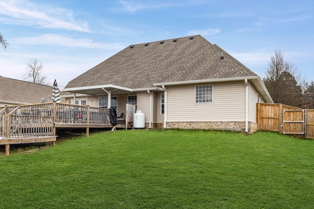 back of house with a deck, a shingled roof, a lawn, and fence