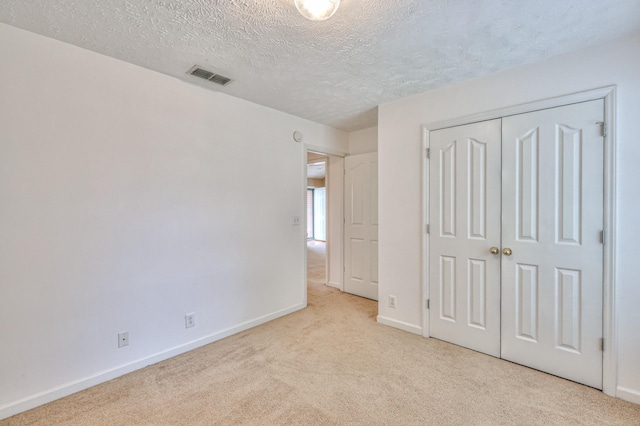 unfurnished bedroom featuring a textured ceiling, carpet flooring, visible vents, baseboards, and a closet